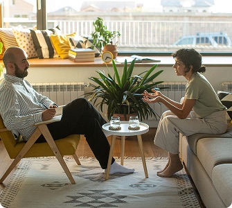 A counselor and a client sitting and talking in a bright, plant-filled treatment room.