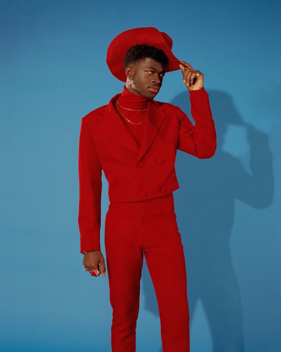 Lil Nas X photographed in a red suit against a blue backdrop.